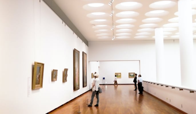 Visitors exploring an art gallery, admiring paintings on the walls as they walk through the gallery